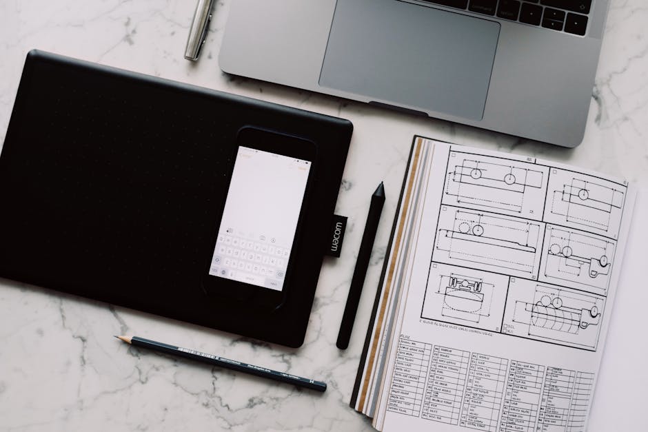 A modern workspace featuring a drawing tablet, smartphone, laptop, and design documents on a marble desk.