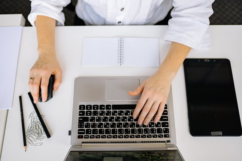 Top view of an office workspace with a laptop, tablet, and hands typing. Ideal for business and technology themes.