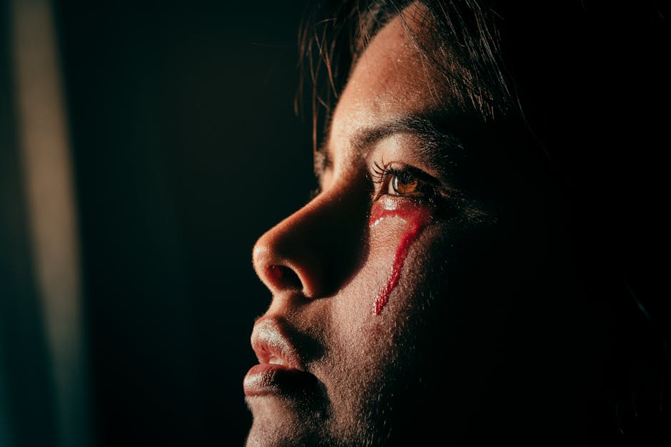 Close-up portrait of a woman with artistic light and red liquid resembling tears, evoking emotion and sorrow.