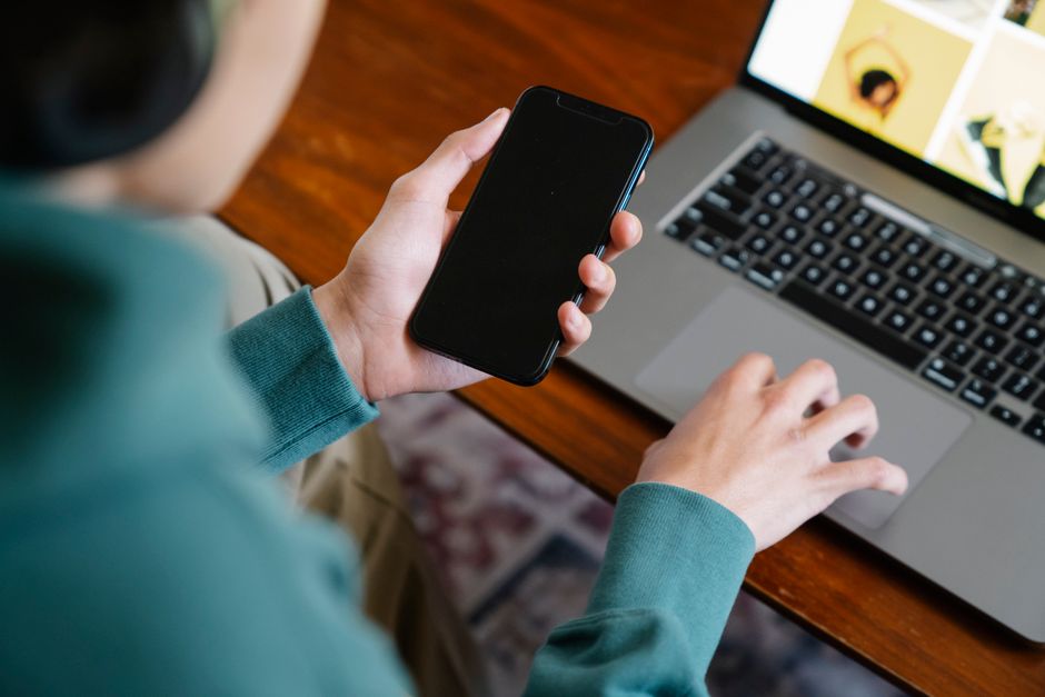 Close-up of a person multitasking using a smartphone and laptop, symbolizing modern remote work.